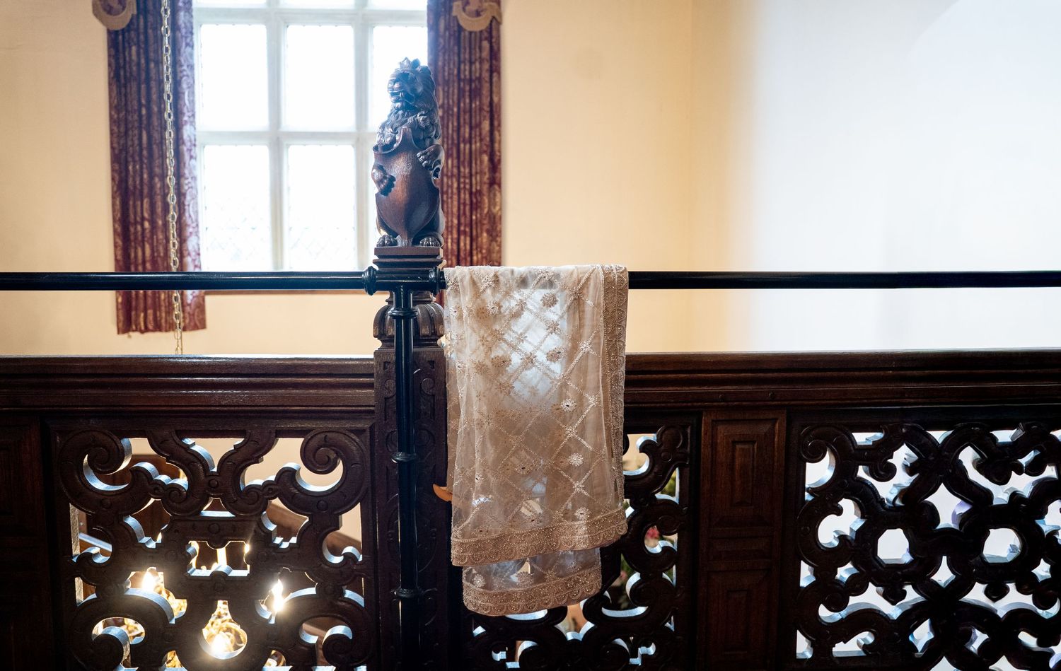 Elegant fabric draped over ornate wooden railing with decorative cutwork panels near a sunlit window.