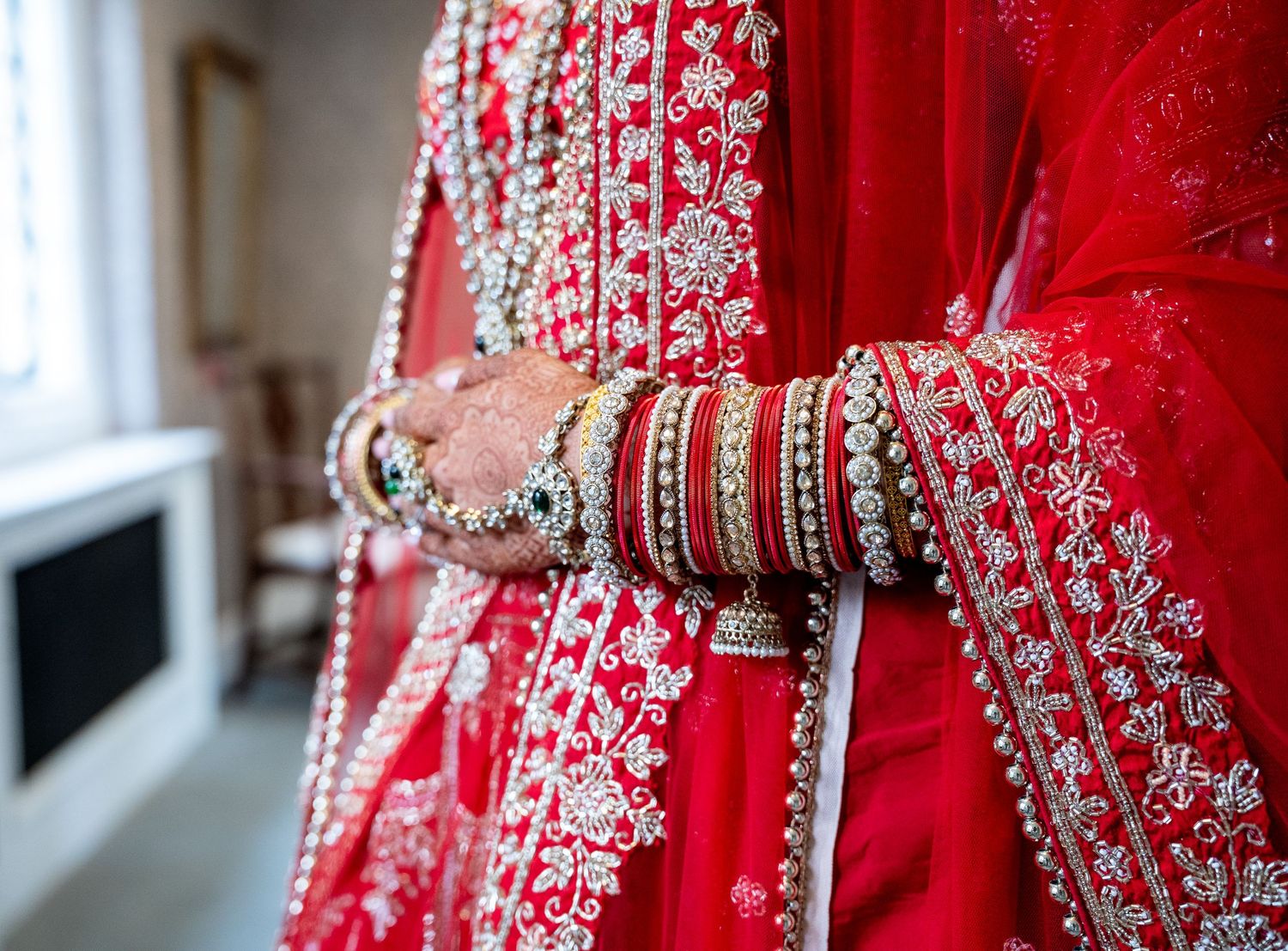Close-up of Indian bride's red embroidered lehenga with gold and red wedding bangles.