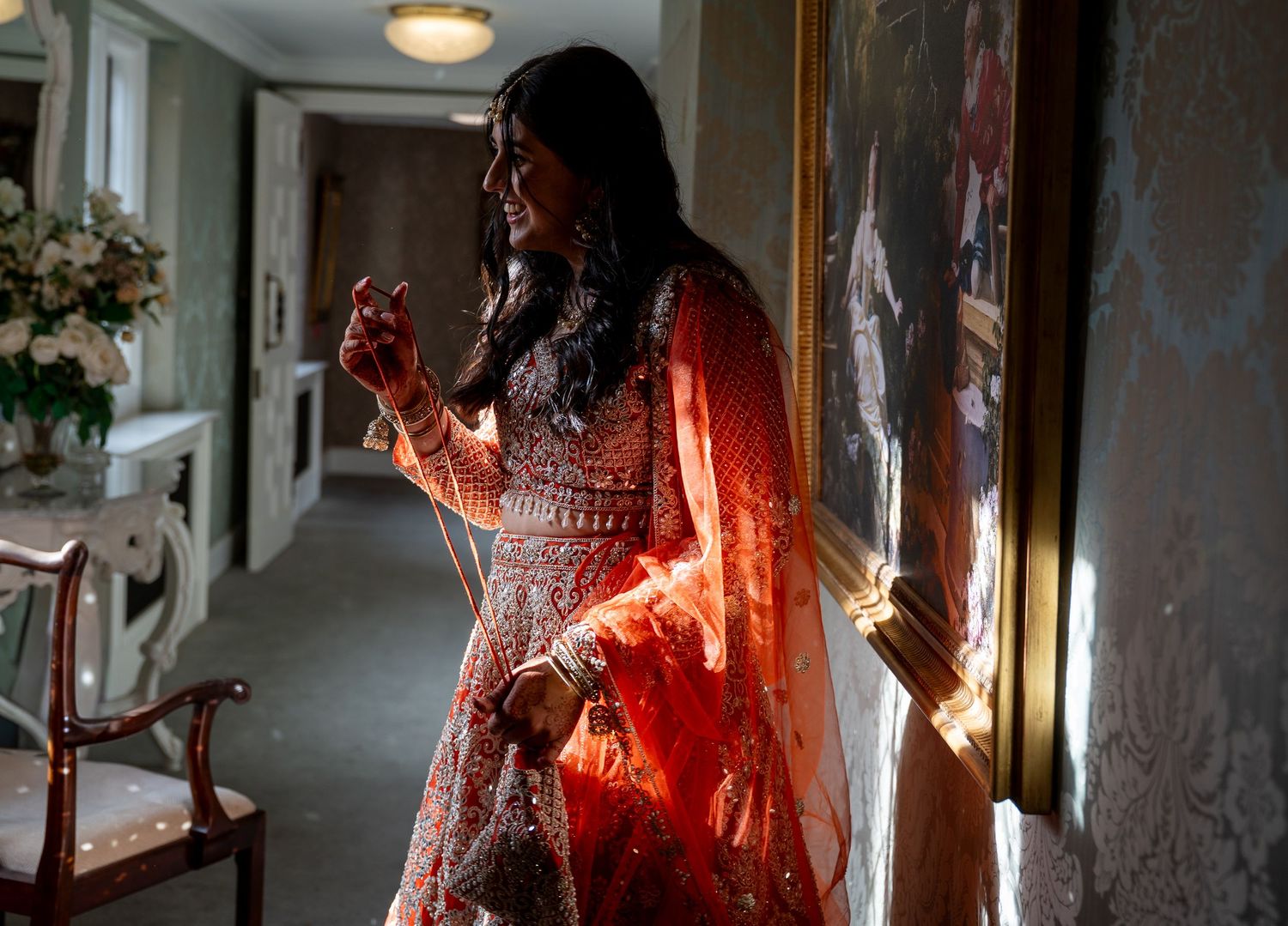 Indian bride in vibrant red embroidered lehenga standing in elegant hotel corridor.