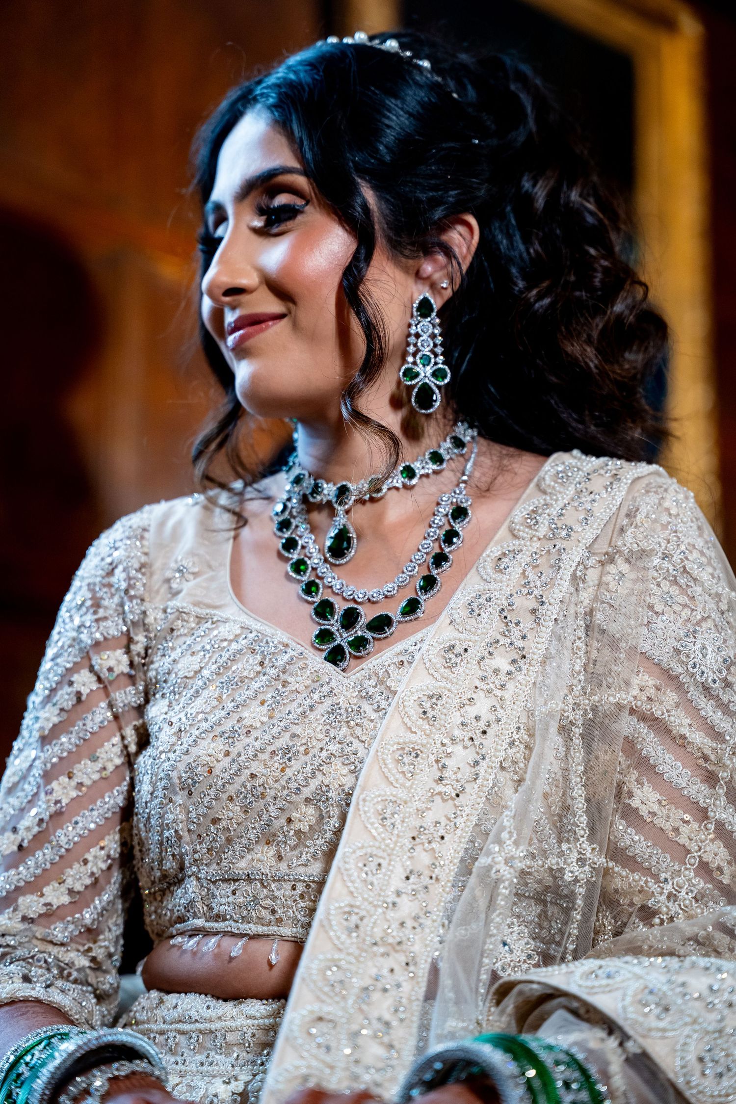Indian bride wearing white embroidered lehenga with stunning emerald and diamond jewelry set.