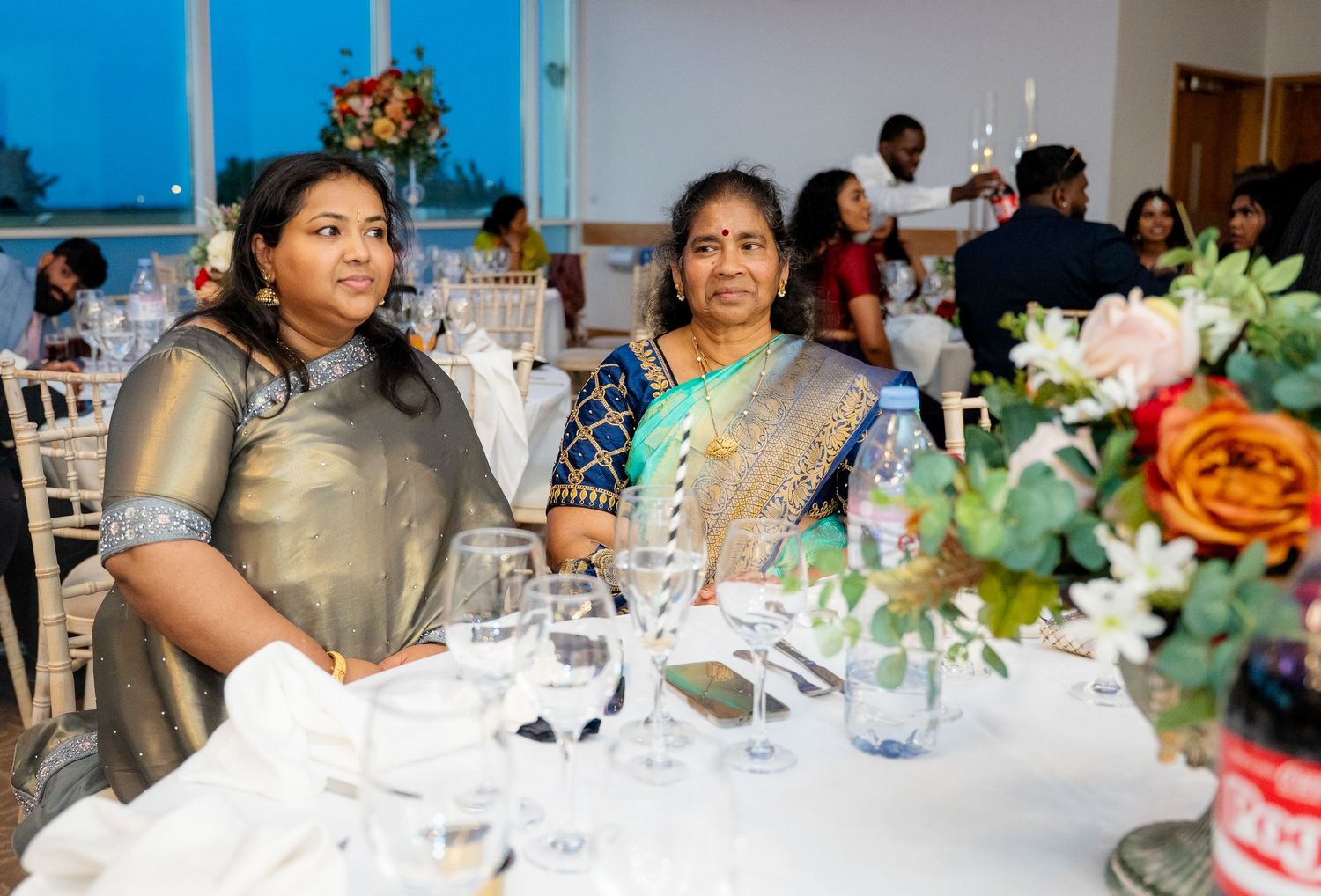 Two women in traditional Indian sarees seated at an elegantly decorated banquet table.