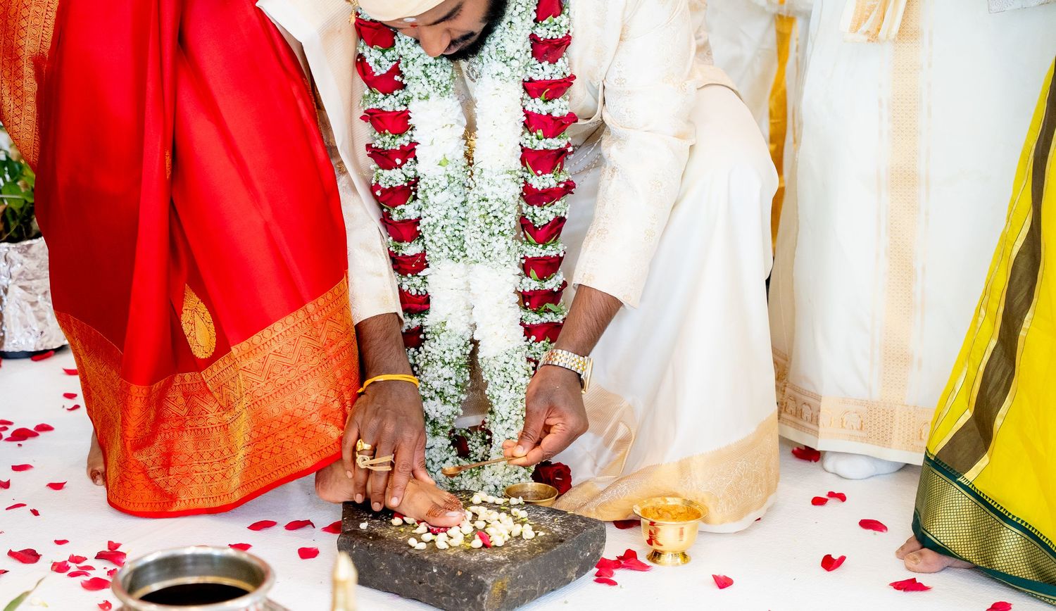 Close-up of Hindu wedding couple performing sacred ritual with offerings on stone at ceremony.