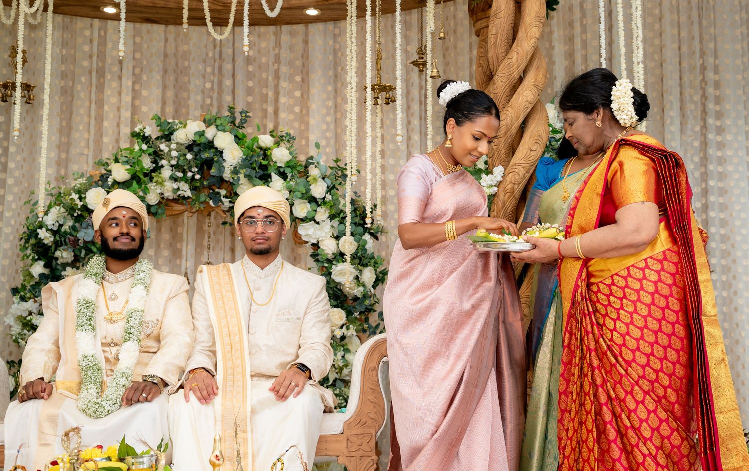 Traditional South Asian wedding ceremony with groom and guests in colorful attire, floral backdrop.