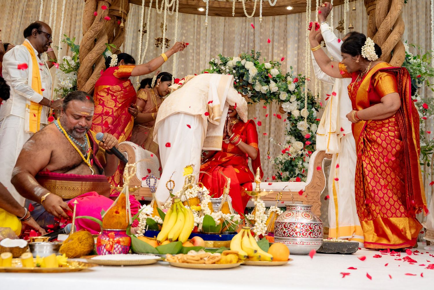 Rose petals shower over bride and groom during traditional South Indian Hindu wedding ceremony at mandap.