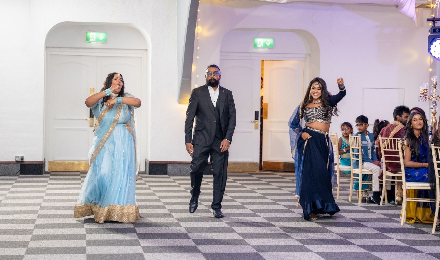South Asian wedding guests performing a choreographed dance entrance in traditional attire on checkered floor.