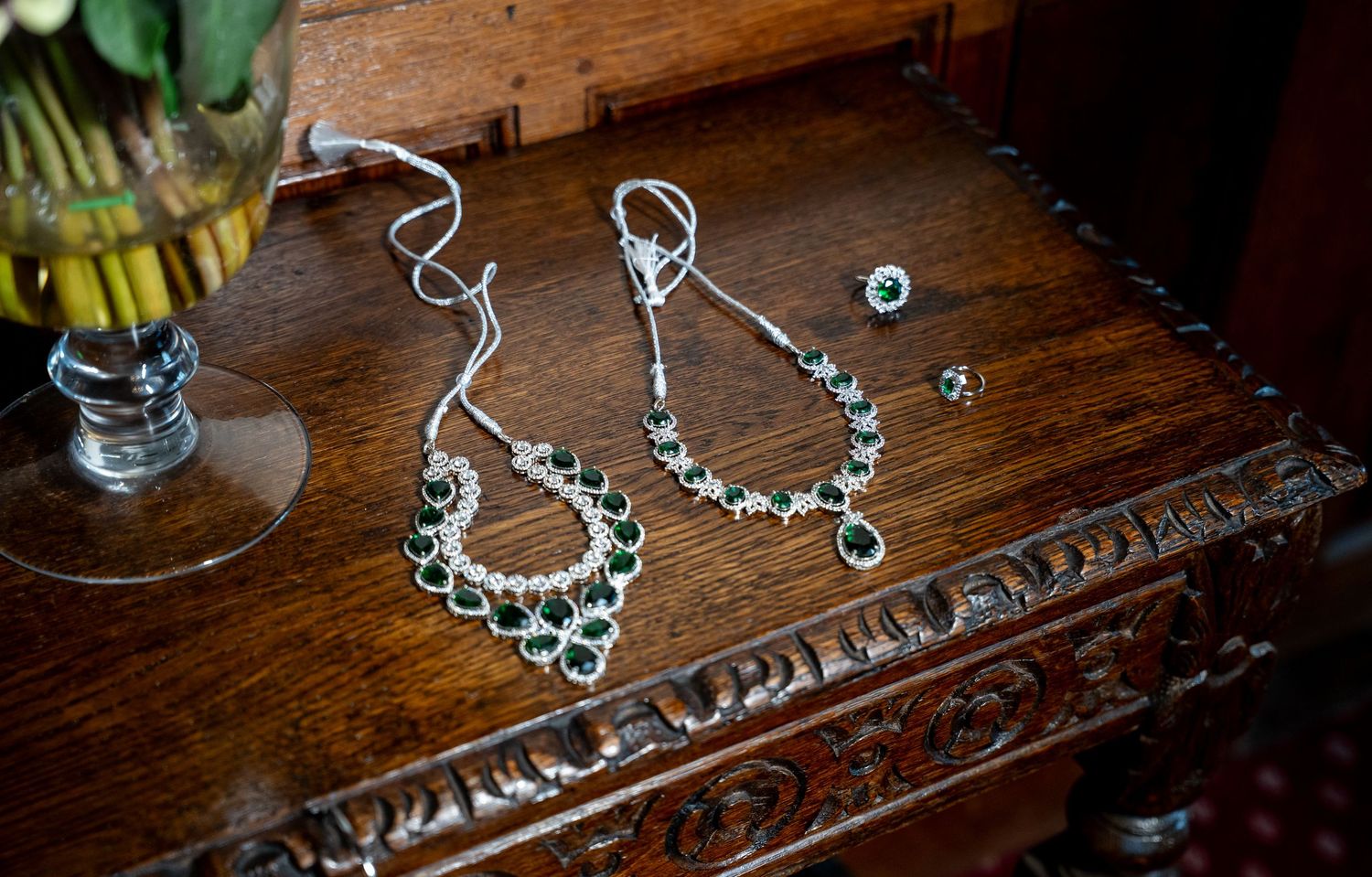 Elegant emerald and diamond bridal jewelry set displayed on antique wooden furniture.