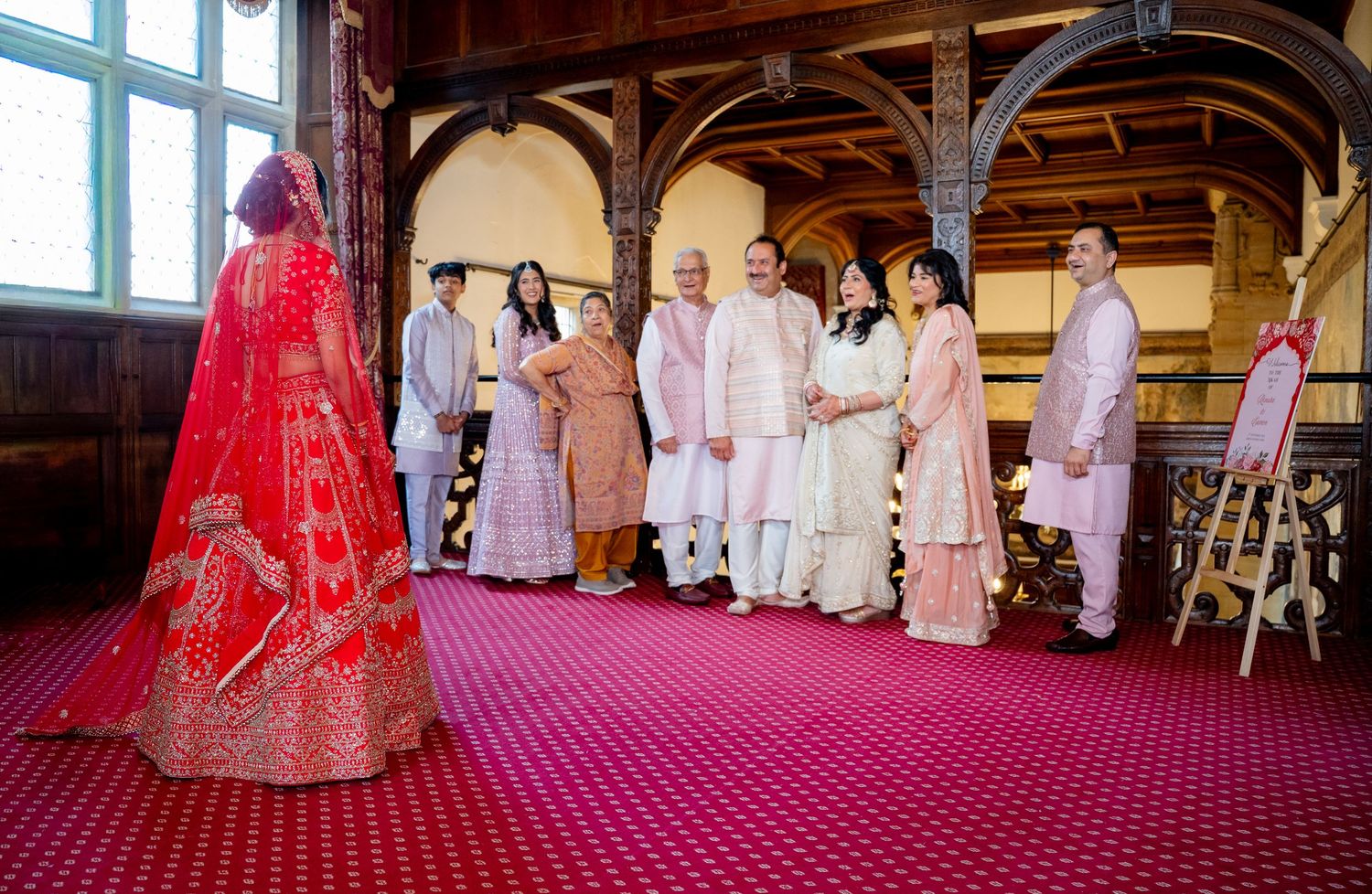 Indian wedding family portrait with bride in red lehenga and guests in pink traditional attire.