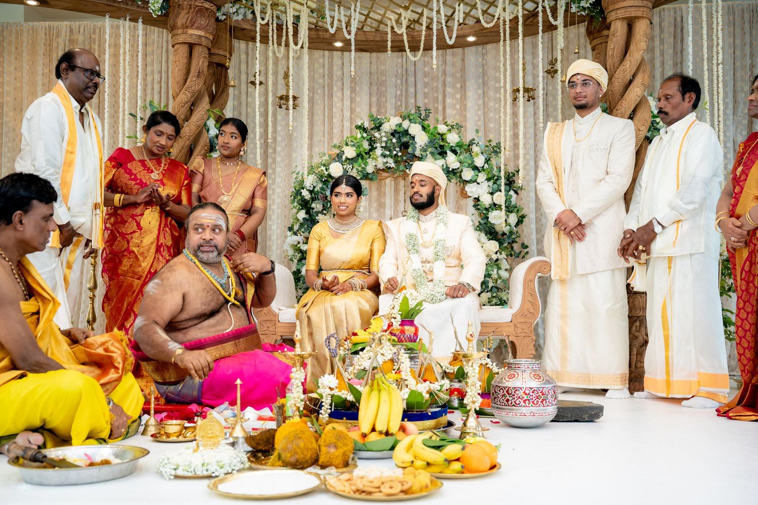 Traditional South Indian wedding ceremony with bride and groom seated at decorated mandap surrounded by family and priest.