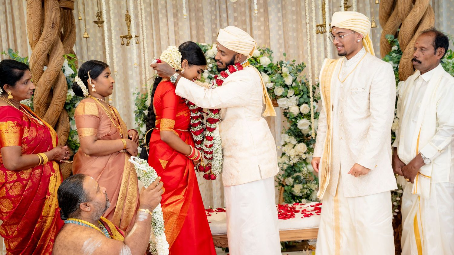 Bride and groom exchange garlands during a traditional South Indian Hindu wedding ceremony on a decorated stage.