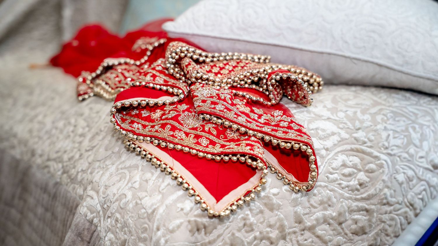 Red and gold embroidered Indian bridal lehenga laid on a white quilted bed.