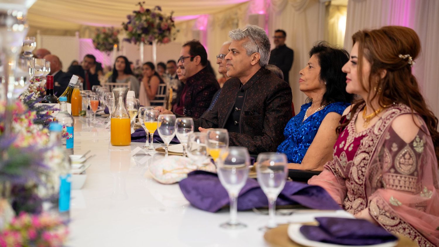 Guests seated at an elegantly decorated banquet table with purple accents at a formal wedding reception.