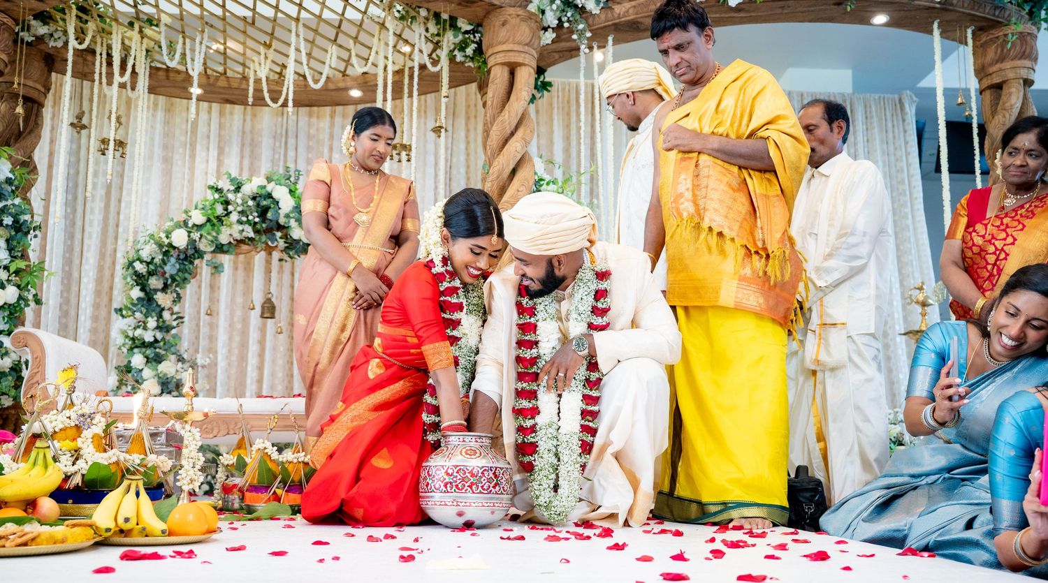 South Indian wedding couple performing traditional rituals at ornate mandap with priest and family.