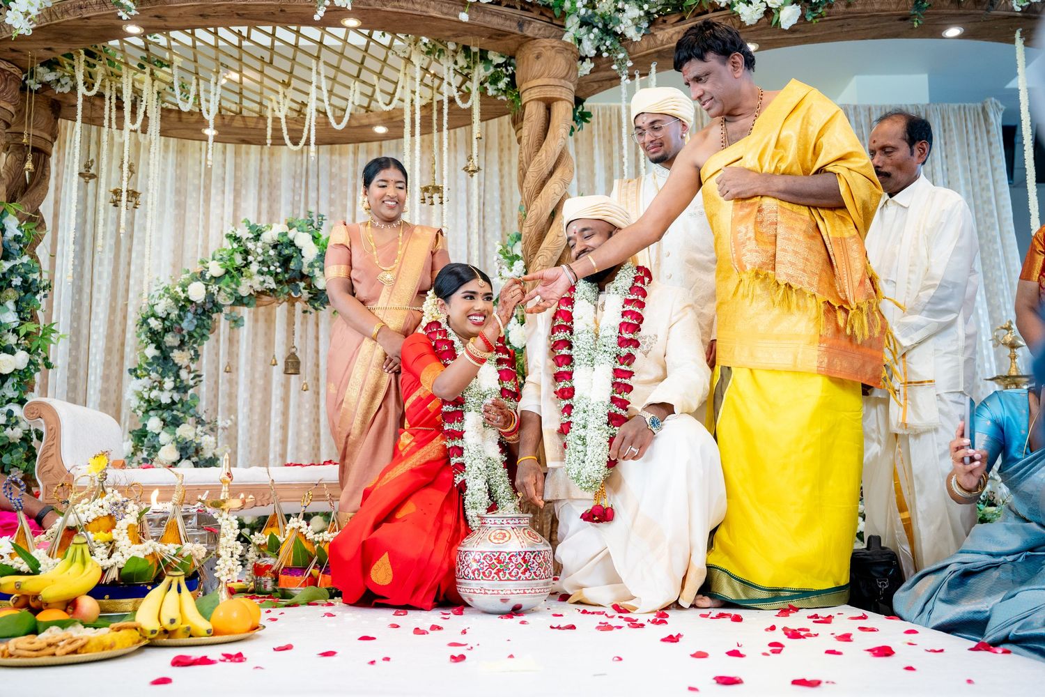 Priest performs sacred rituals as bride and groom sit together during a colorful Hindu wedding ceremony.