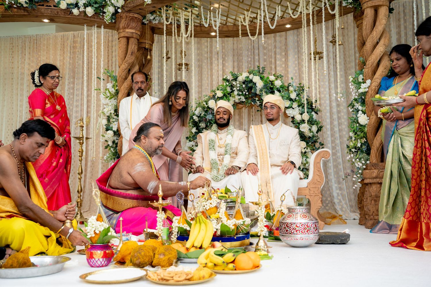 Hindu priests conduct traditional wedding rituals surrounded by offerings and family in vibrant sarees.