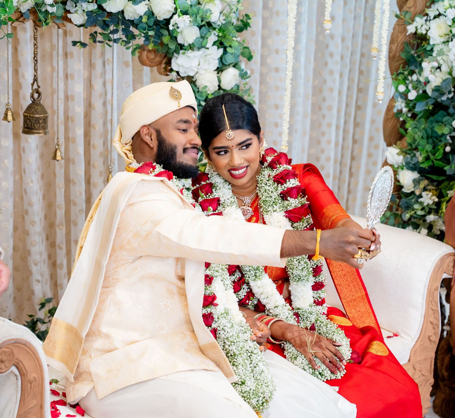 Bride and groom pose together wearing floral garlands at elegant South Indian wedding celebration.