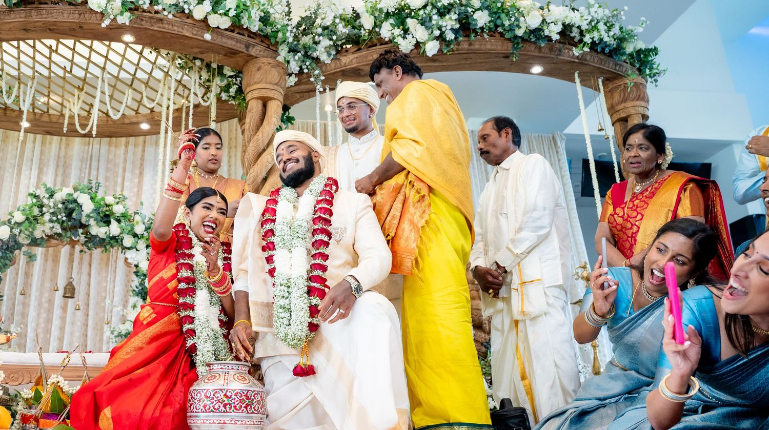 Bride in red saree and groom in white sherwani celebrate Hindu wedding under decorated mandap.