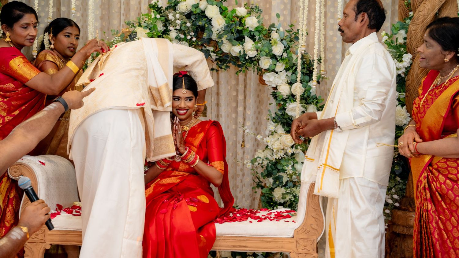 South Indian bride in red silk saree smiling during traditional Hindu wedding ceremony at floral mandap.