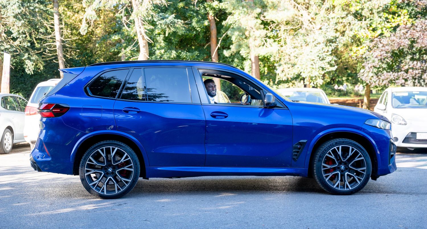 Blue BMW X5 SUV parked on suburban street with driver visible through window.