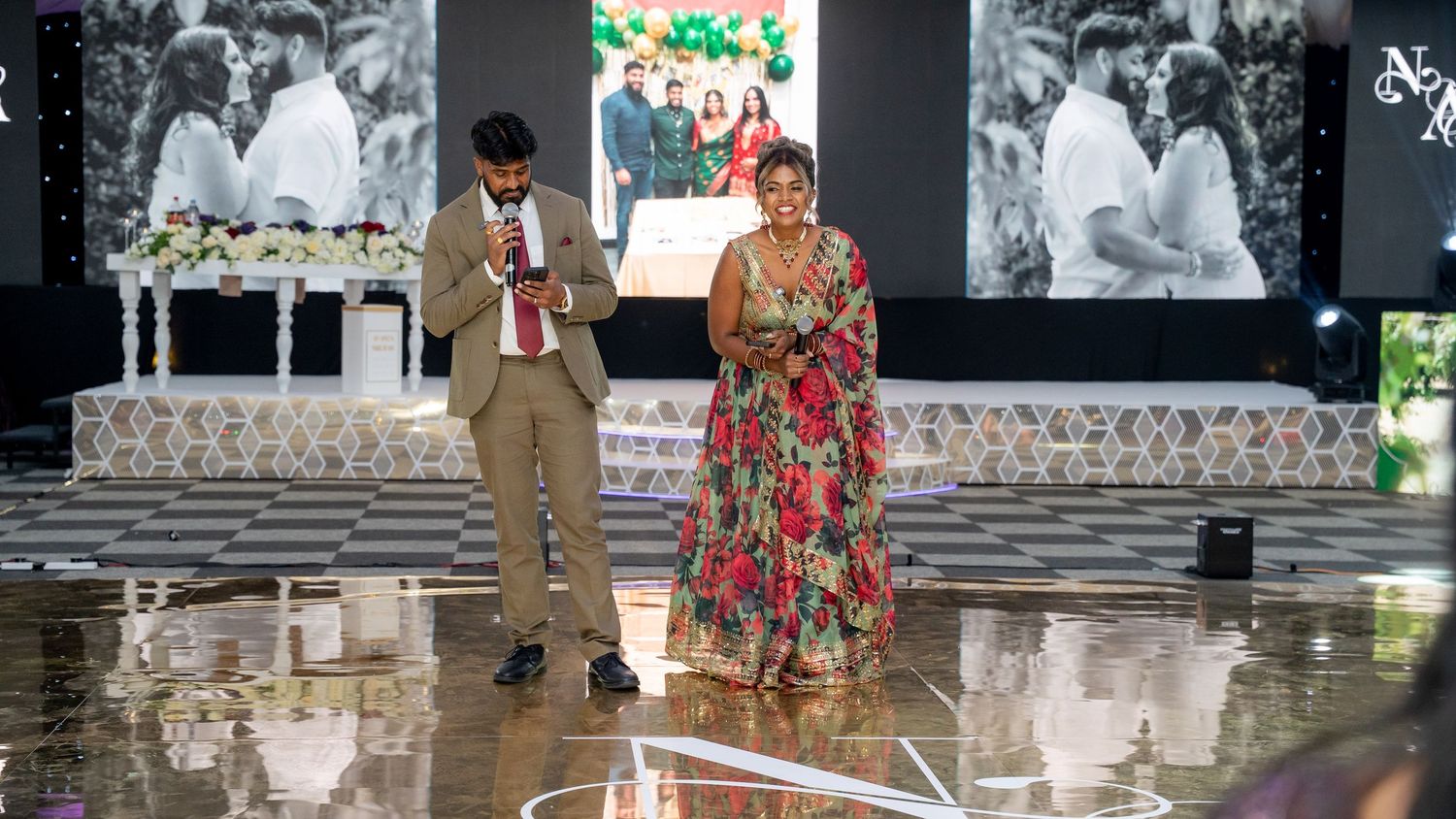 Man and woman in traditional Indian outfits presenting on a wedding reception dance floor.
