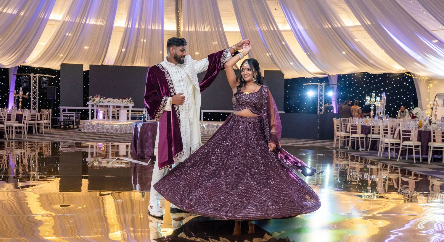 A couple dances elegantly at an Indian wedding reception, the bride spinning in a stunning purple lehenga.