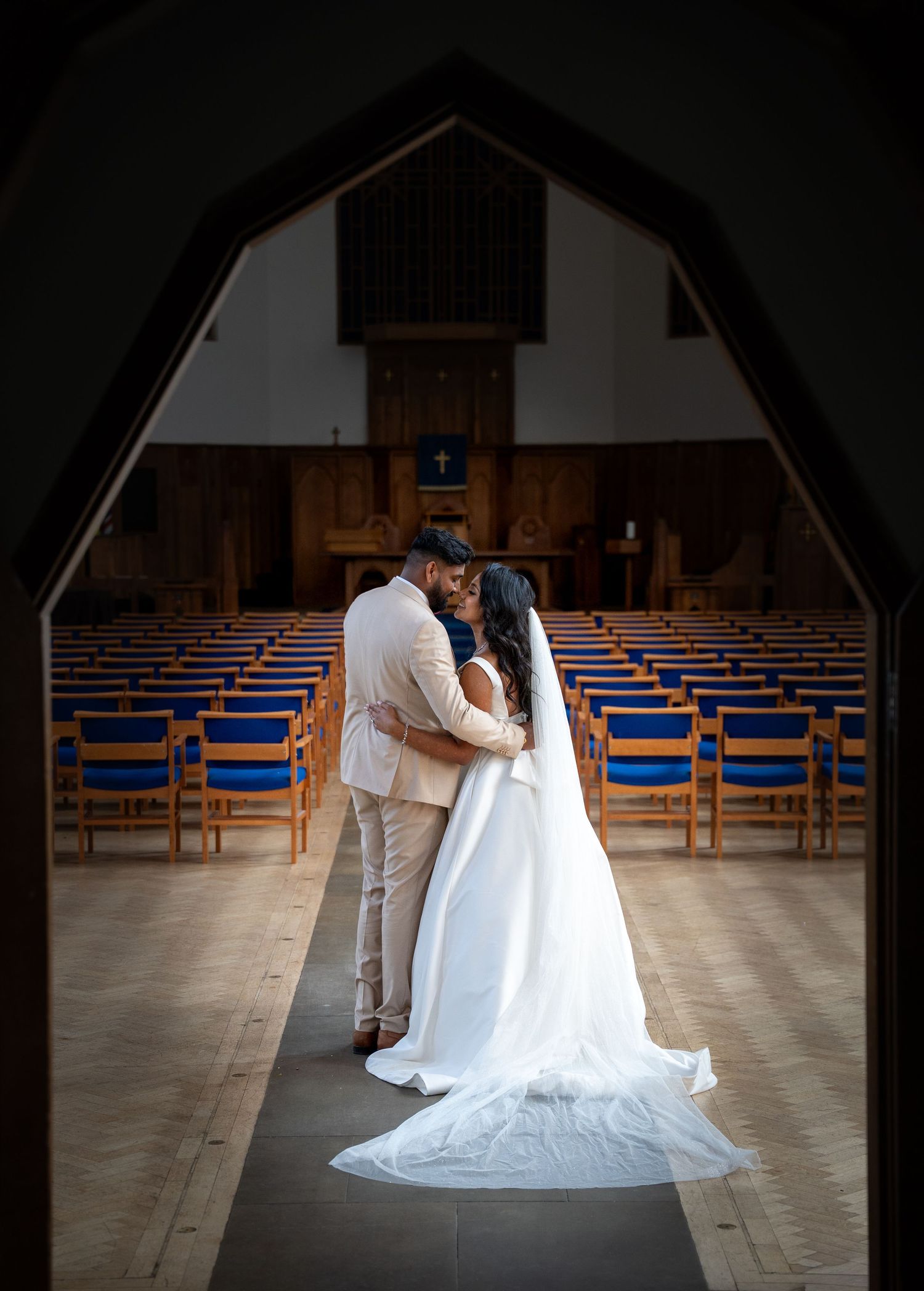 Couple sharing romantic kiss in church aisle framed by gothic arch with blue chairs.