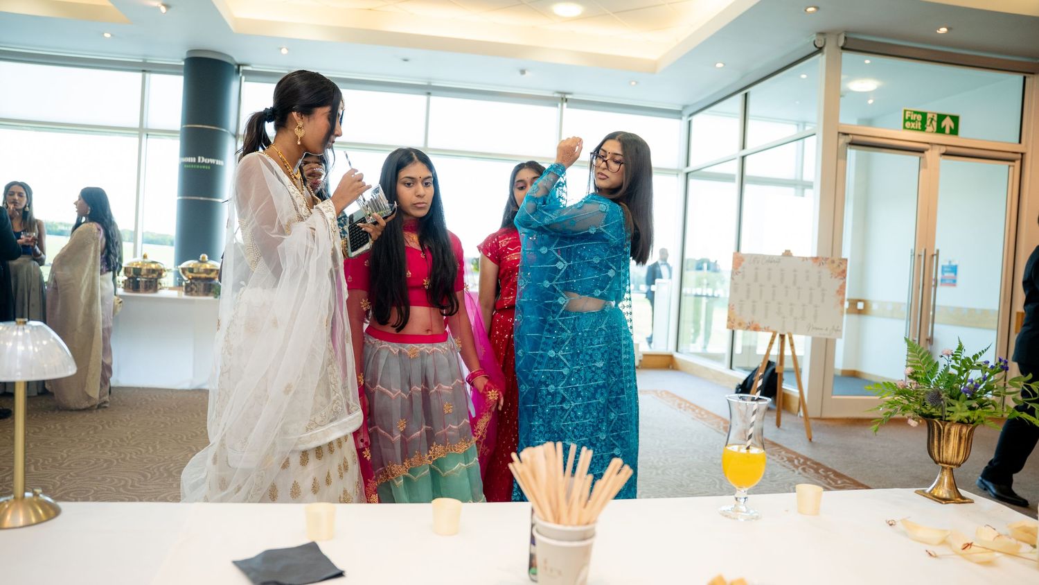 Women in colorful Indian traditional attire socializing at a wedding reception venue.