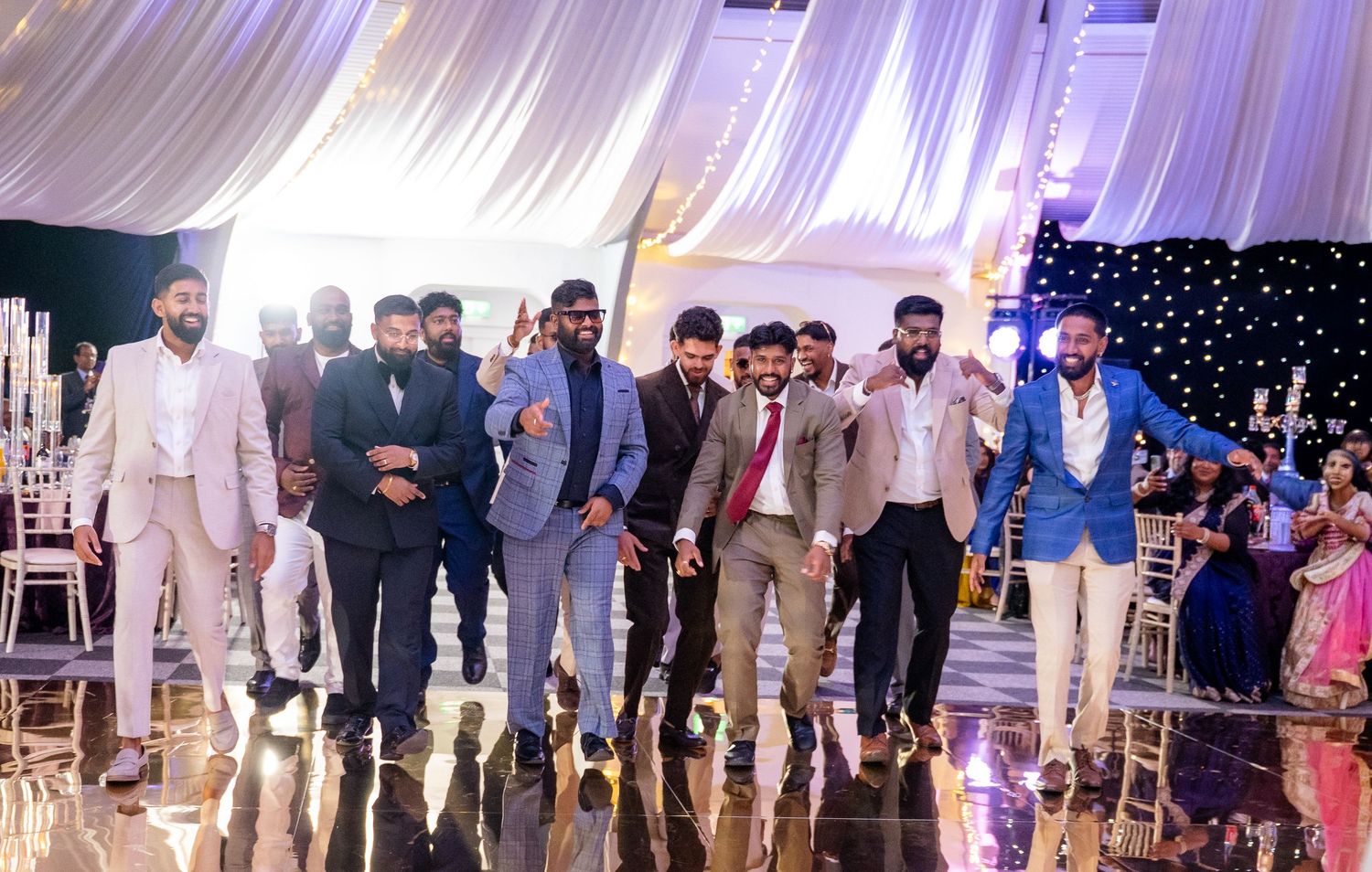 Group of men in suits walking confidently across a decorated wedding reception dance floor.