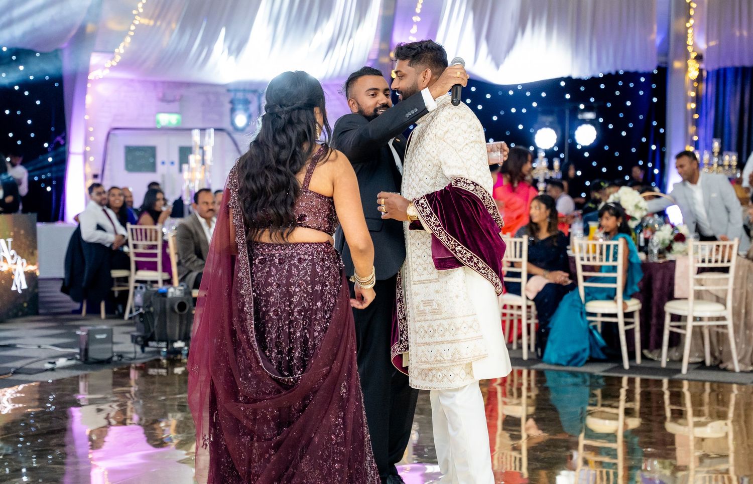 Guests dancing at an elegant Indian wedding reception in a decorated banquet hall with twinkling lights.