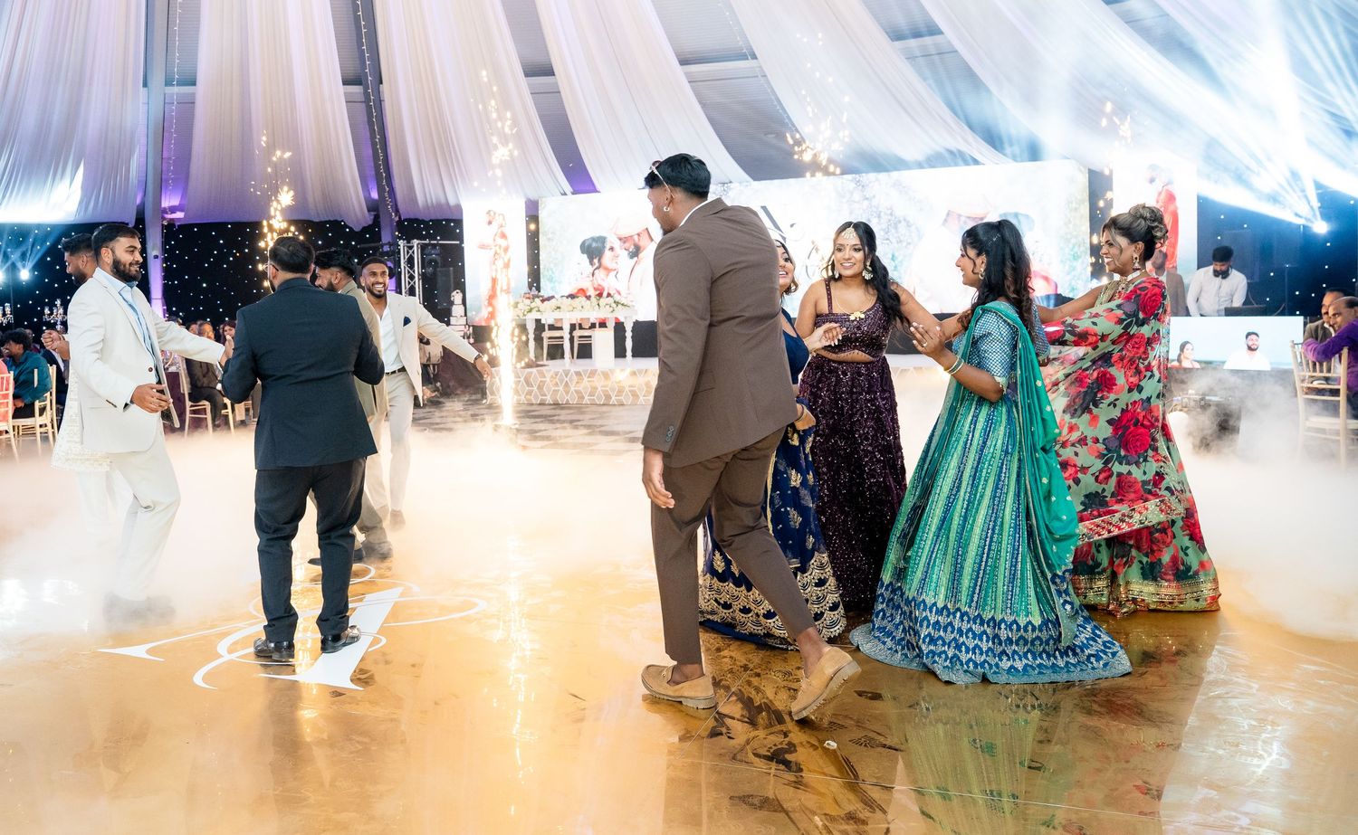 Guests dancing at an elegant Indian wedding reception under a white draped tent with sparkling lights.