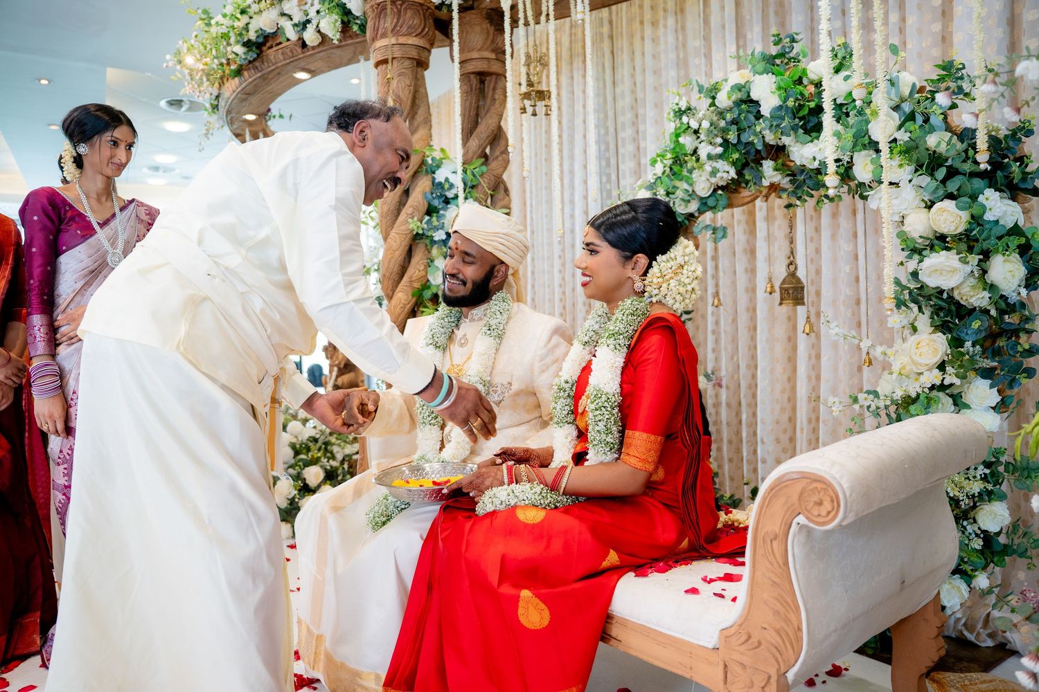 Family elder performing traditional blessing ritual for Hindu bride and groom at decorated wedding mandap.