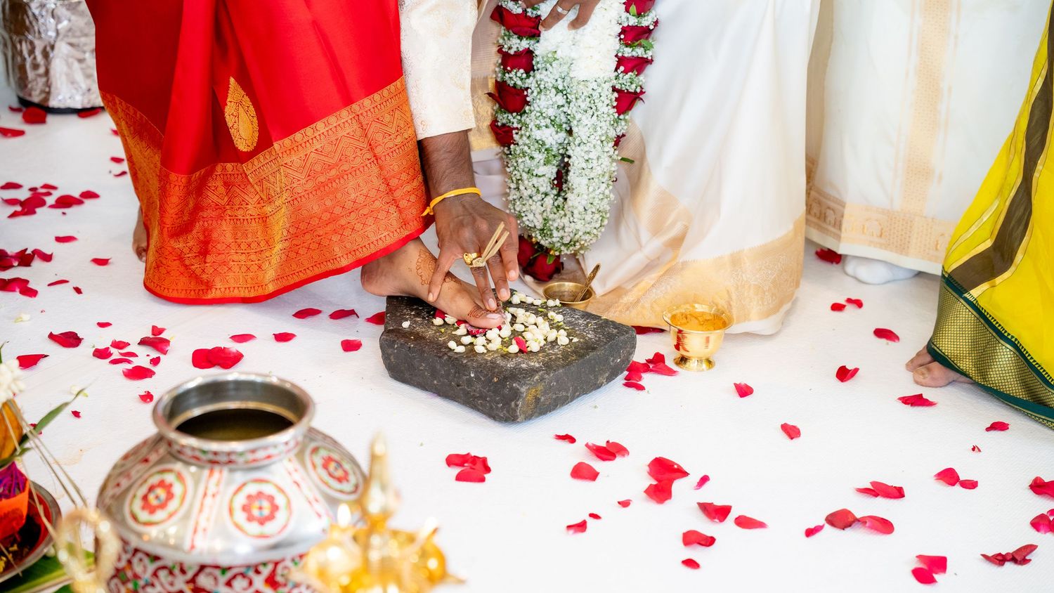 Detail shot of Hindu wedding ritual with flower offerings on stone plate and rose petals.