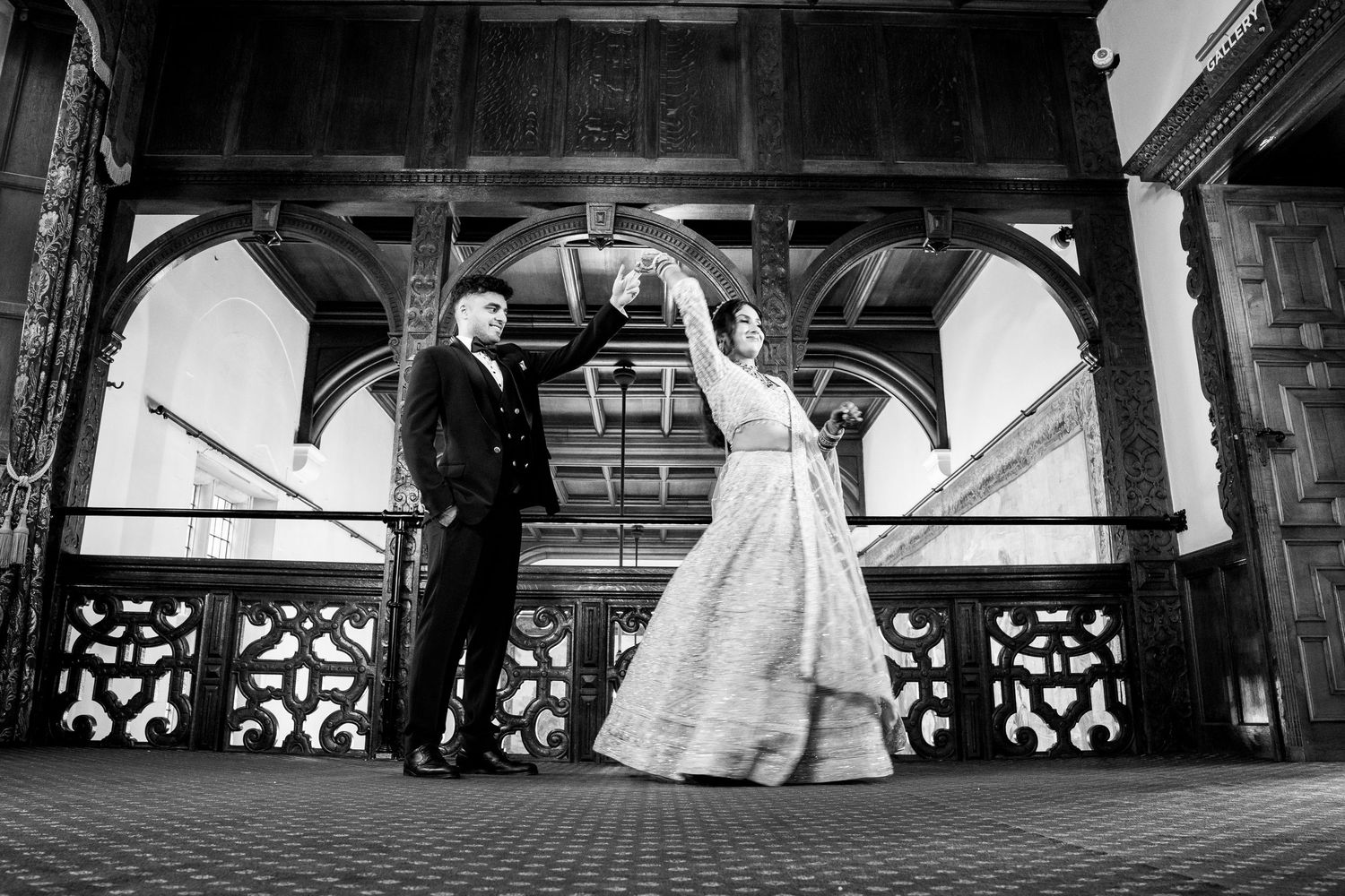Black and white photo of bride and groom dancing on ornate wooden staircase at elegant wedding venue.