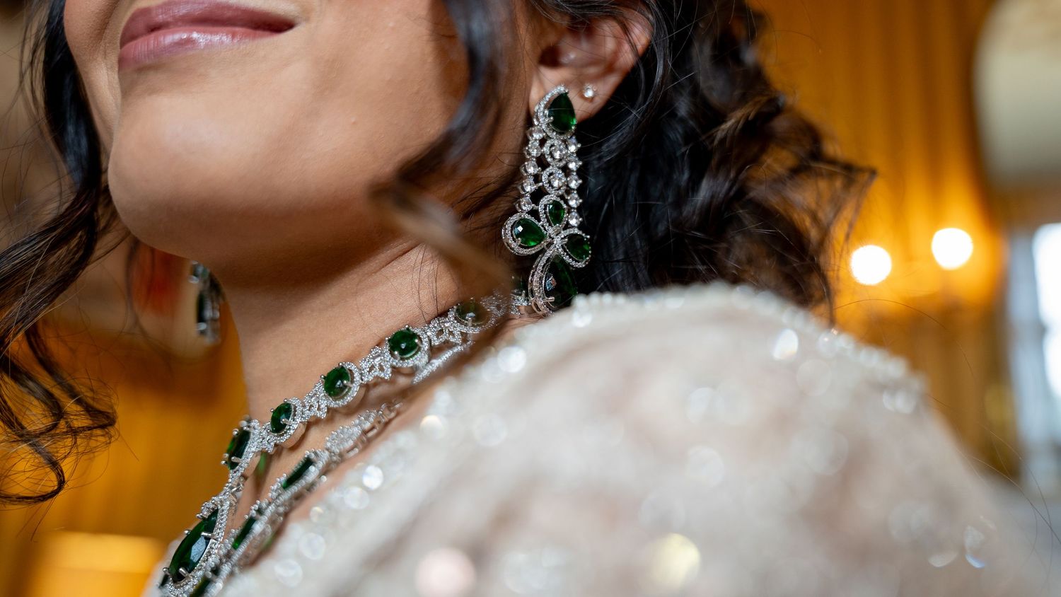 Detailed close-up of emerald and diamond chandelier earrings and necklace on Indian bride.