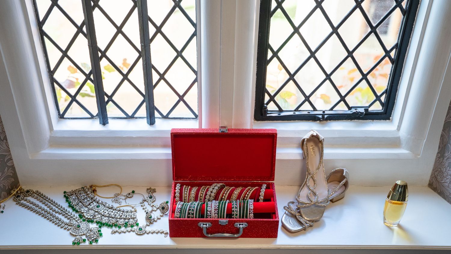 Bridal bangles and jewelry displayed in red box on windowsill with diamond-patterned leaded glass.