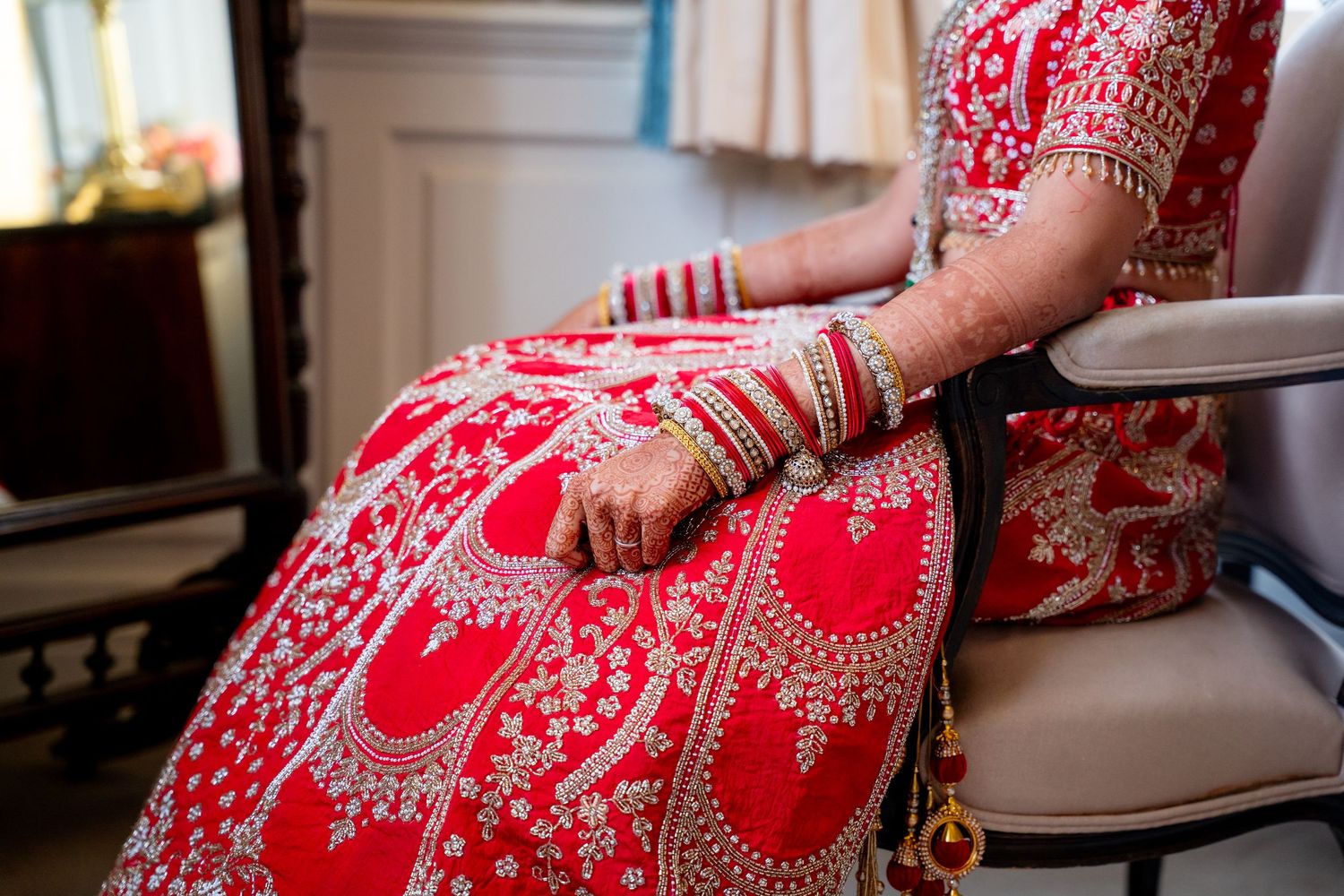 Close-up of Indian bride in red embroidered lehenga with mehndi hands and bangles.