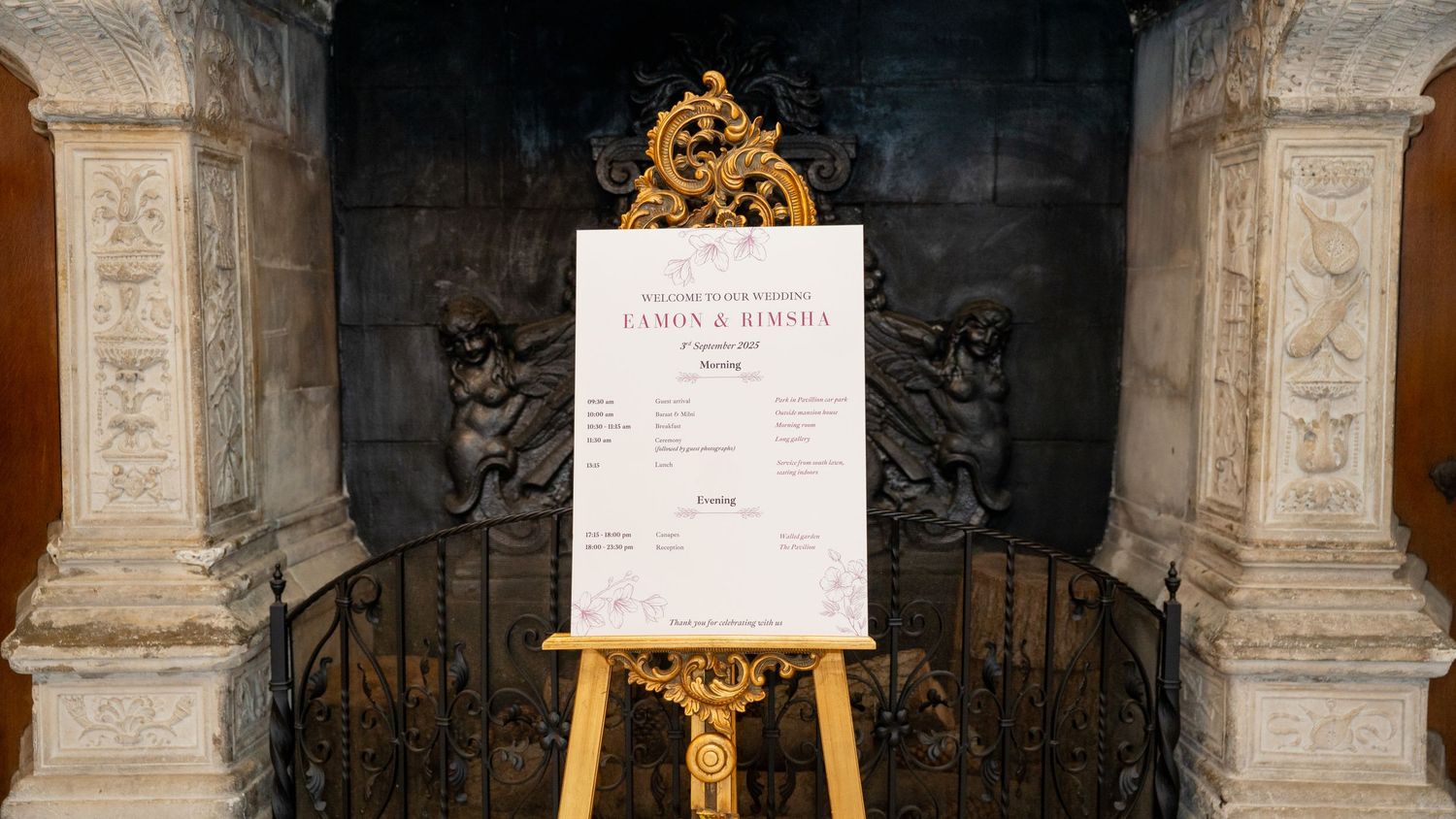 Elegant wedding seating chart on easel with gold ornate frame displayed in front of decorative fireplace.