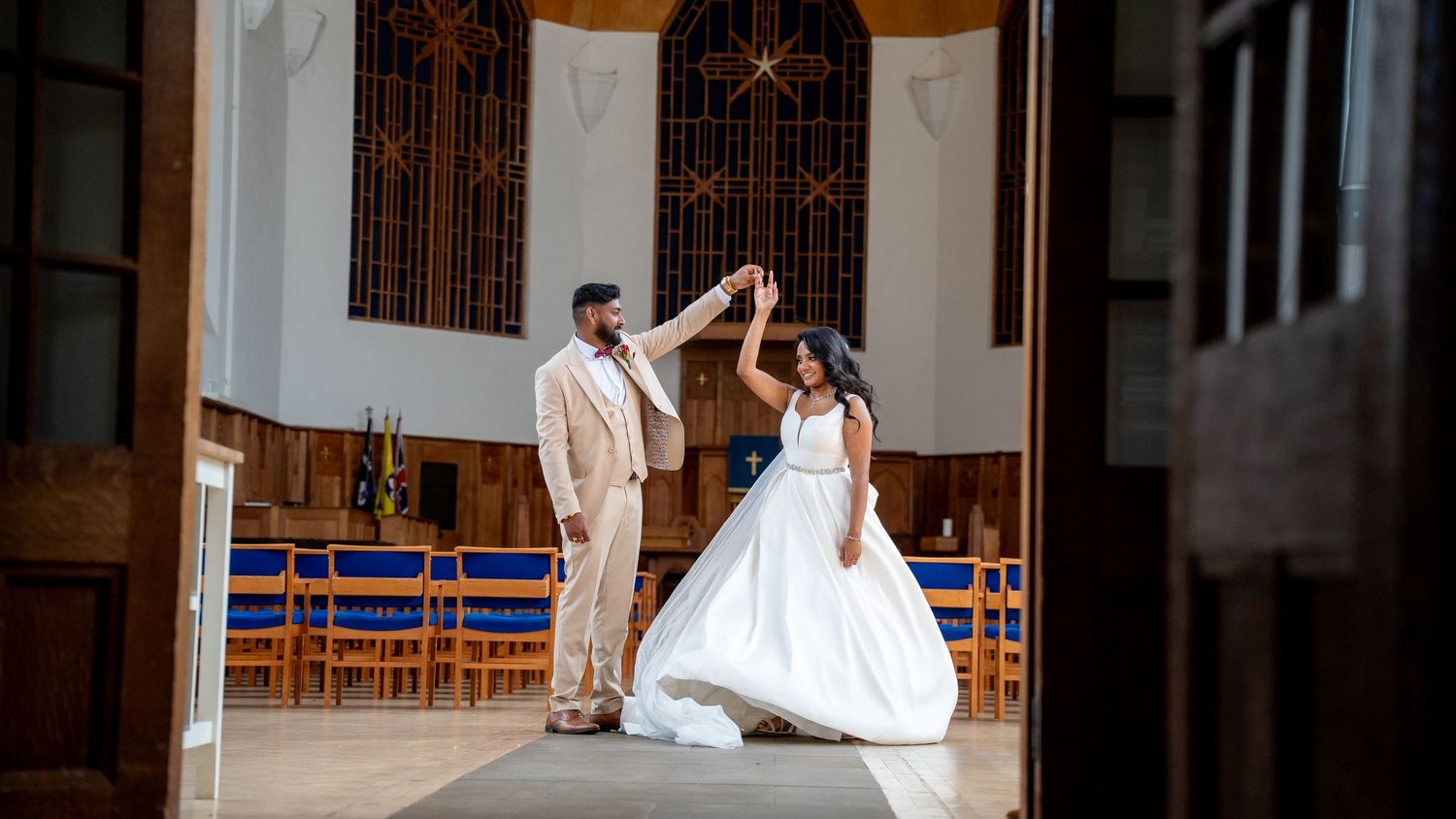 Bride and groom share a first dance in an elegant church, with the groom twirling his bride in a white gown.