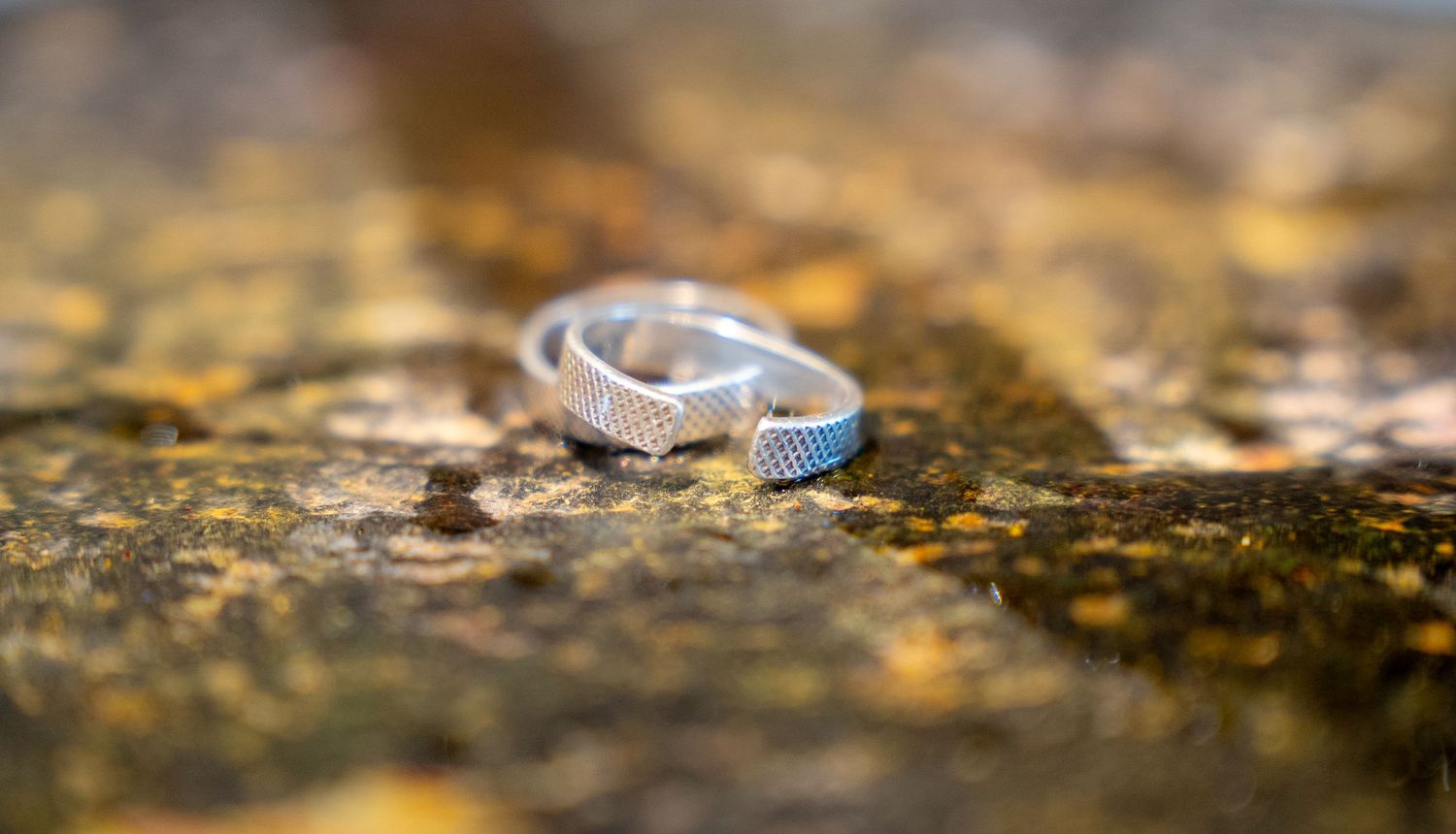 Silver textured wedding ring resting on a mossy stone surface with shallow depth of field.