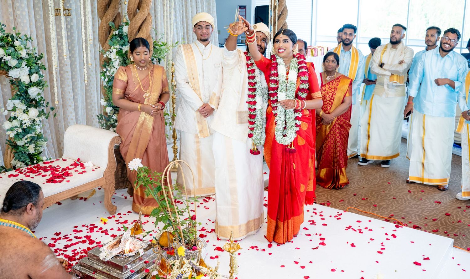 Groom raises hand in blessing during Hindu wedding ceremony with bride in red saree.