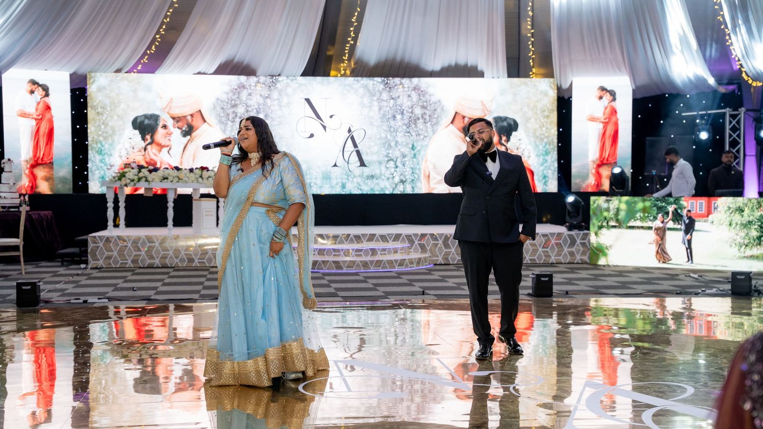 Male and female singers perform on stage at an Indian wedding reception in an outdoor marquee venue.