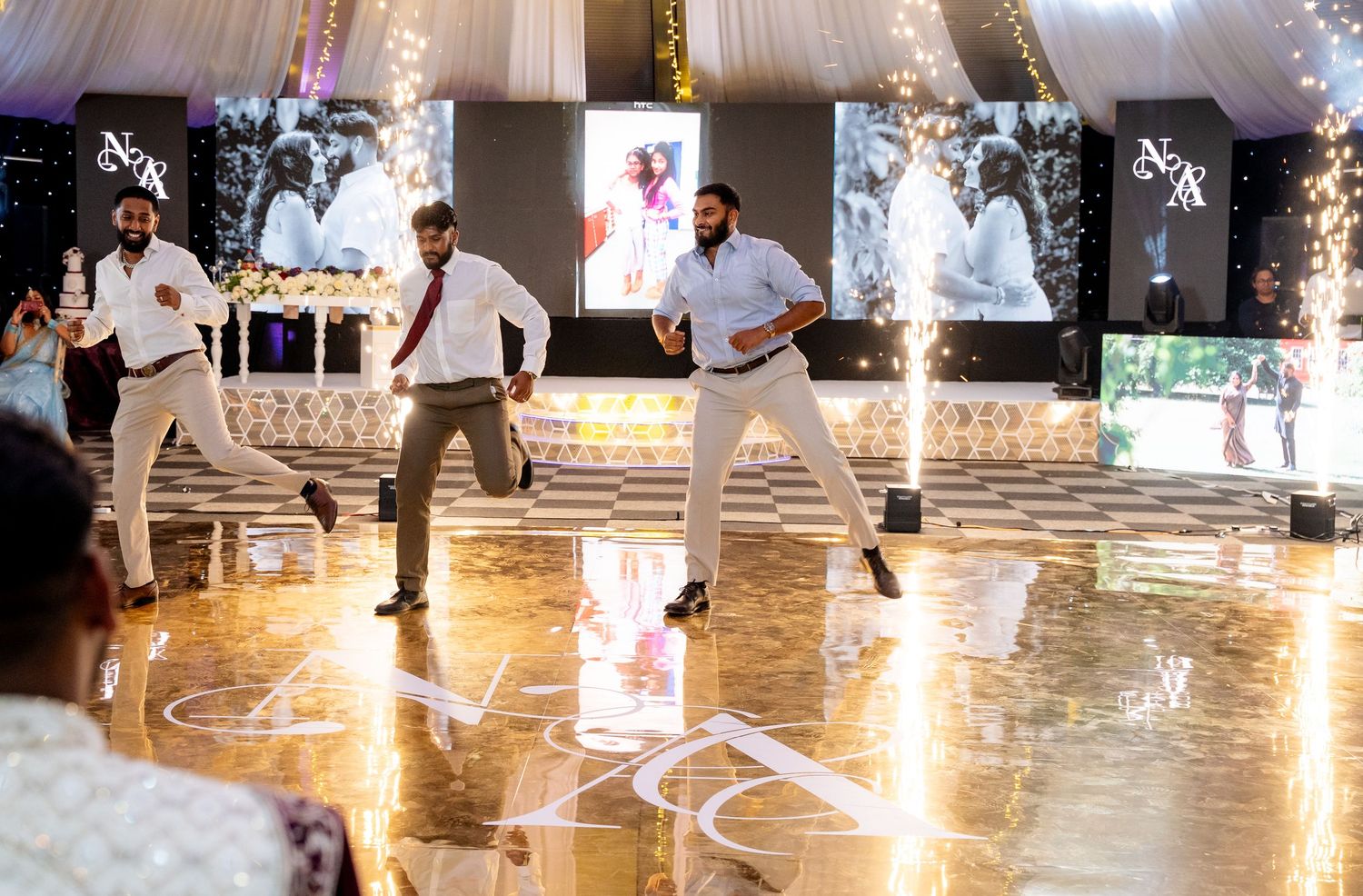 Groomsmen performing an energetic dance routine on a decorated wedding reception dance floor with sparkling lights.