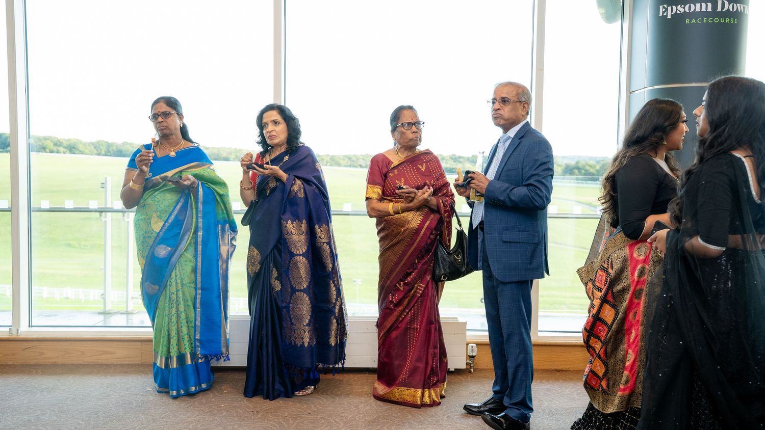 Group of guests in colorful Indian sarees and formal wear gathered at a wedding reception.