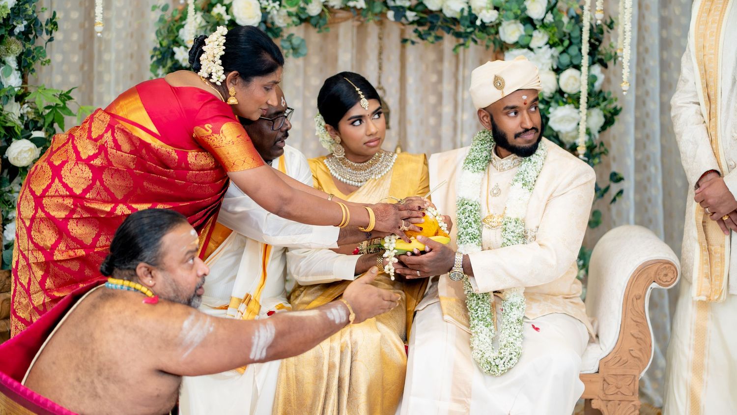 Traditional Hindu wedding with family members performing sacred rituals for couple at floral decorated altar.