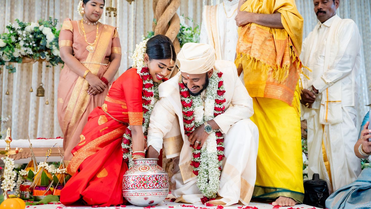 Bride in red saree and groom in white perform traditional South Indian wedding ritual with flower garlands.