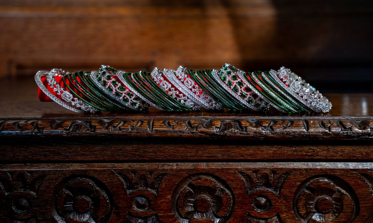 Colorful green and red Indian wedding bangles lined up on an ornately carved wooden surface.