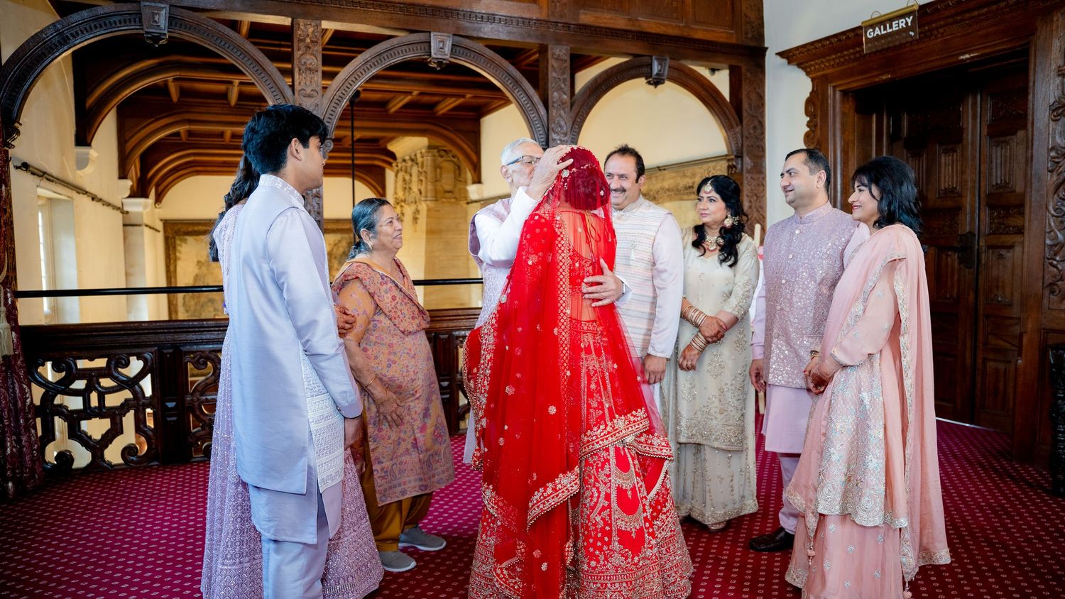 Indian wedding ceremony with bride in red lehenga surrounded by family in traditional attire.
