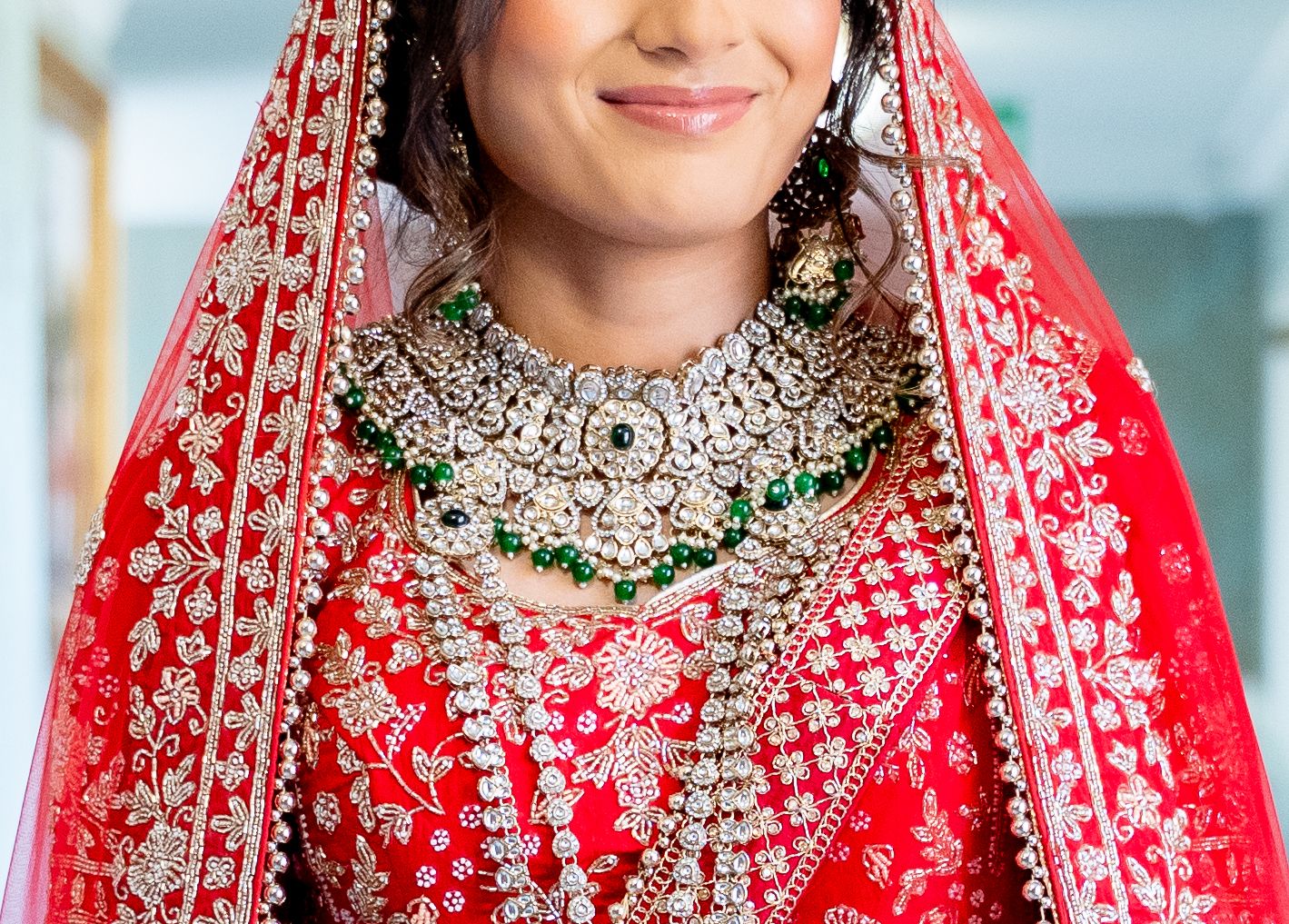Close-up of Indian bride in red lehenga wearing stunning diamond and emerald bridal jewelry.
