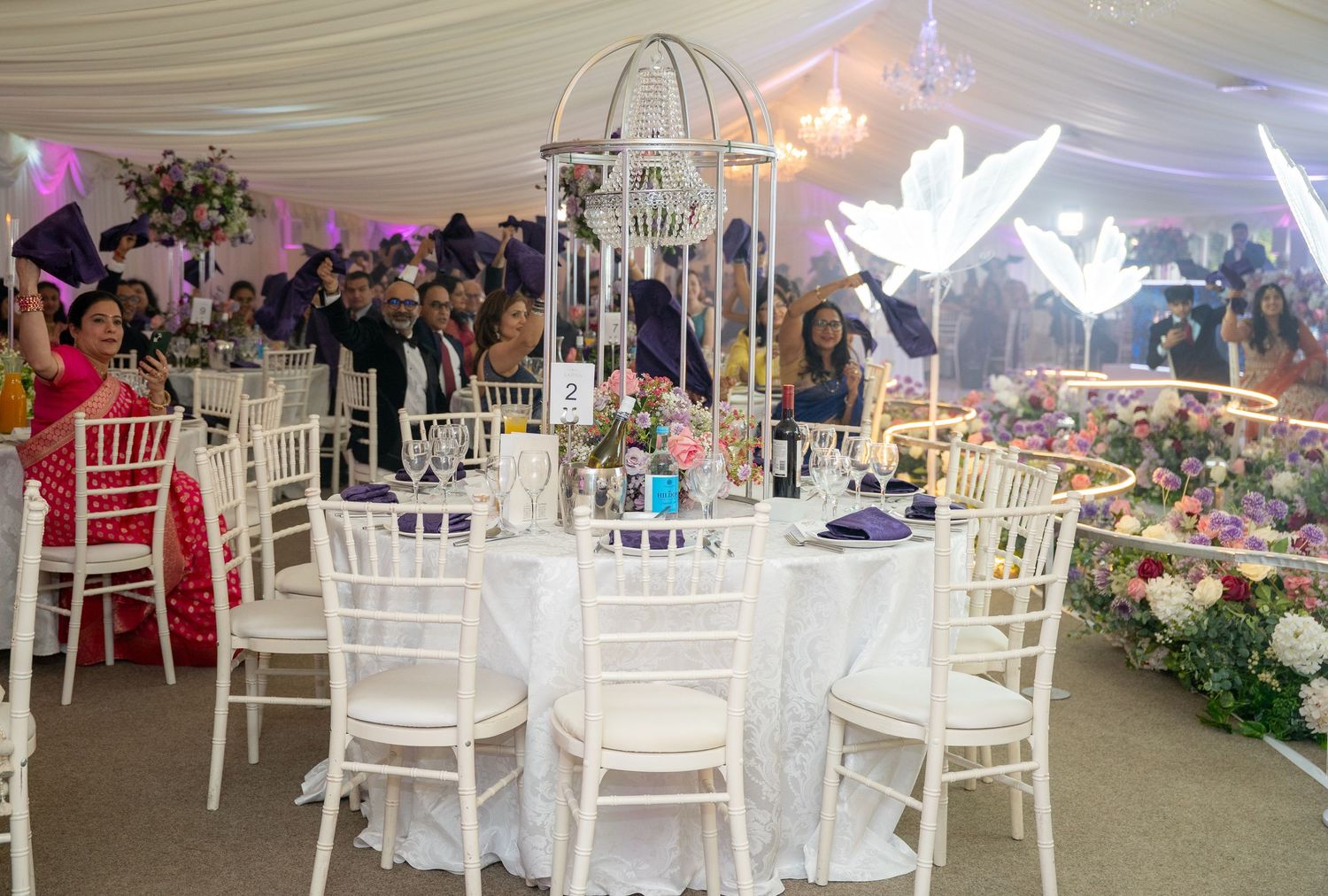 Decorated wedding reception marquee with white Chiavari chairs, round tables, and floral centerpieces.
