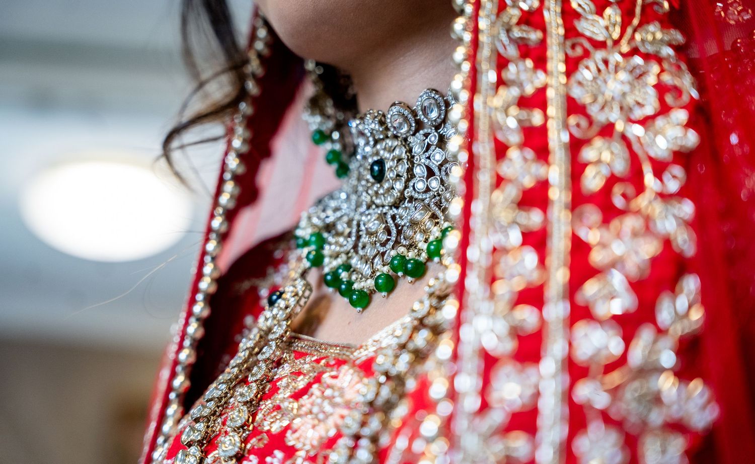 Close-up of Indian bride wearing stunning diamond and emerald necklace with red bridal outfit.