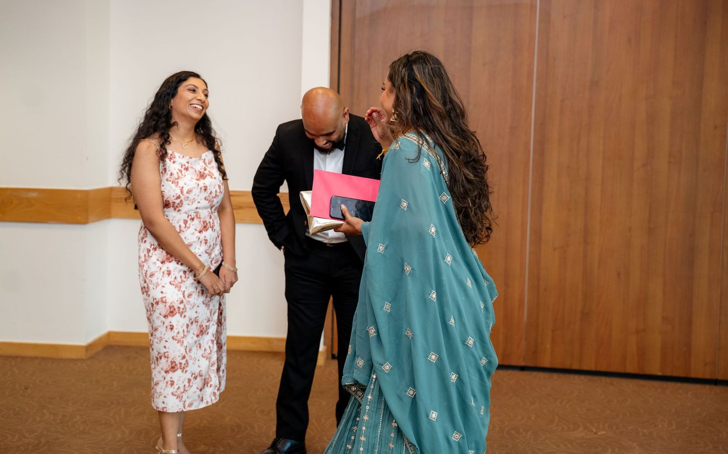 Three guests in formal attire exchanging greetings at an elegant indoor celebration event.